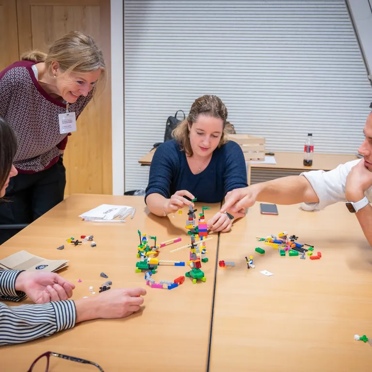 Four people sitting at a table collaboratively building an abstract lego structure